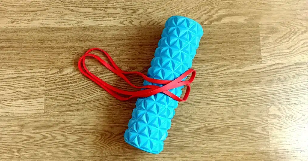 Blue foam roller and red resistance band for a daily mobility routine on a wooden floor.