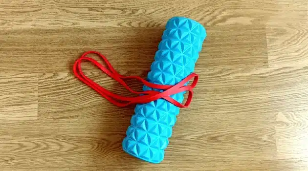 Blue foam roller and red resistance band for a daily mobility routine on a wooden floor.