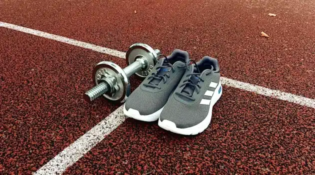 Strength vs cardio after 40 — running shoes and dumbbells on a track